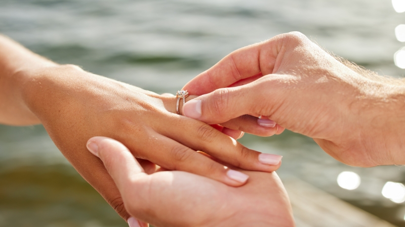 Muškarac stavlja verenički prsten na ruku devojci pored vode