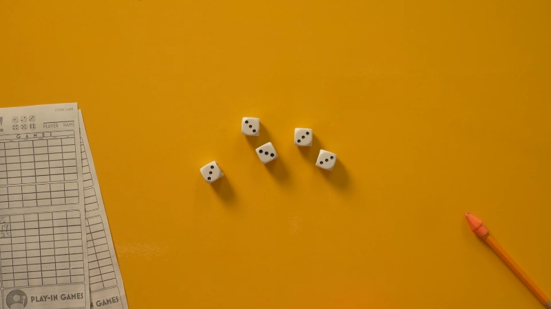 Pet belih kockica na žutoj podlozi pored jamb liste i olovke spremne za upis poena
