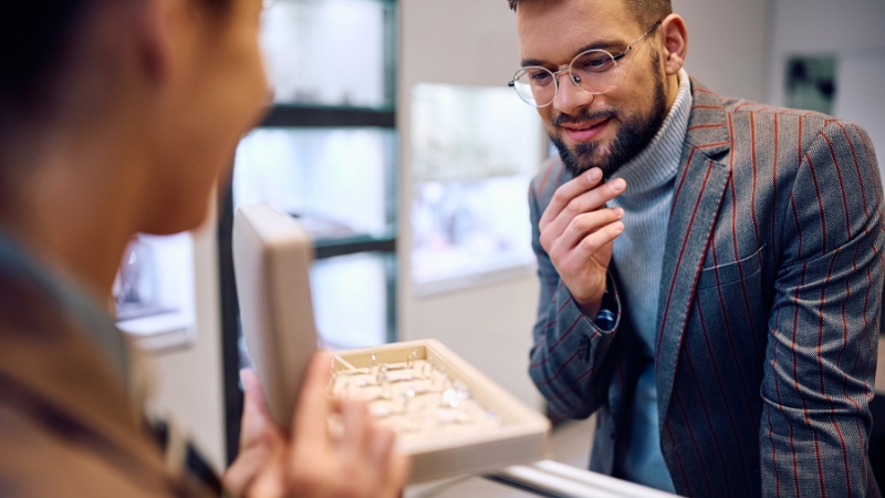 Muškarac u zlatarni pažljivo posmatra vereničke prstenove dok mu prodavačica pokazuje otvorenu kutiju sa različitim modelima