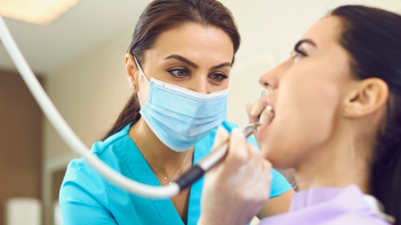 Stomatolog tokom pregleda uklanja naslage sa zuba pacijentkinje u ordinaciji