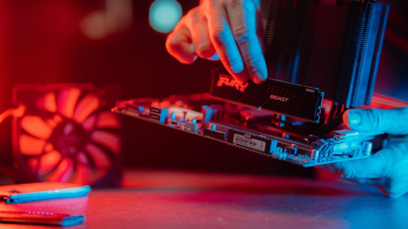 Osoba postavlja RAM memoriju na matičnu ploču pod crveno-plavim osvetljenjem