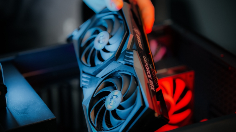 Ruka postavlja grafičku kartu sa dva ventilatora u kućište računara uz crveno osvetljenje u pozadini